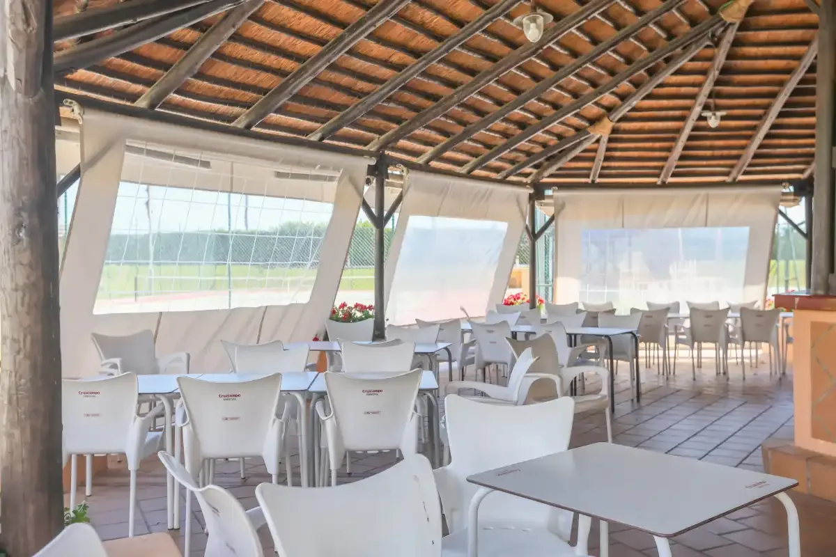 A covered dining area with tables and seating beneath a timber roof.