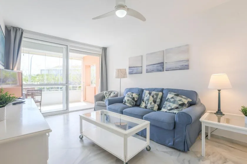 A bright living room with blue seating and a glass-topped coffee table.