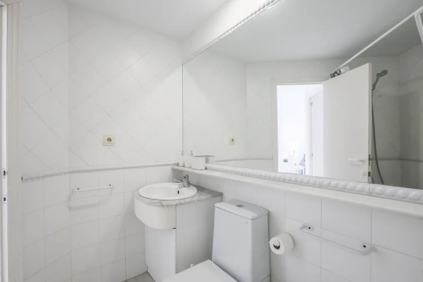 A bright white bathroom with a sink, toilet, and large wall mirror.