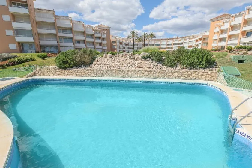 A swimming pool sits in front of apartment buildings and landscaped grounds.
