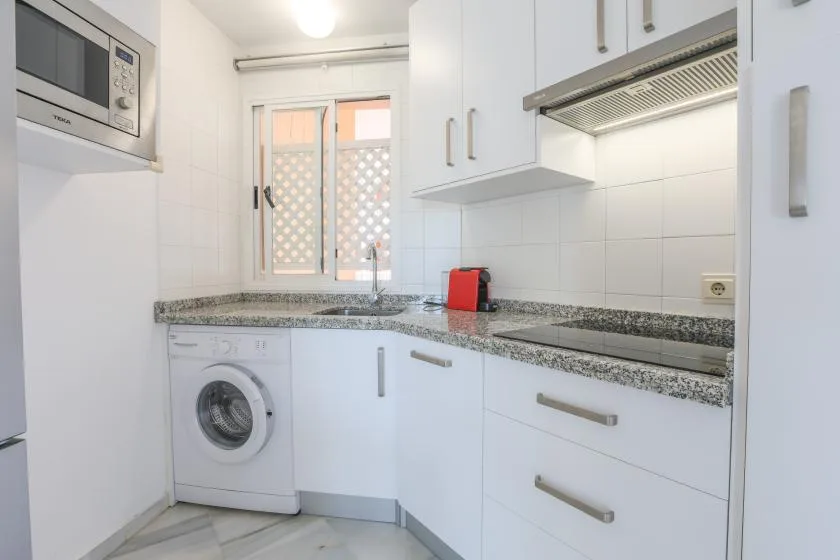 A bright kitchen with white cabinets, a granite countertop, and a washing machine.
