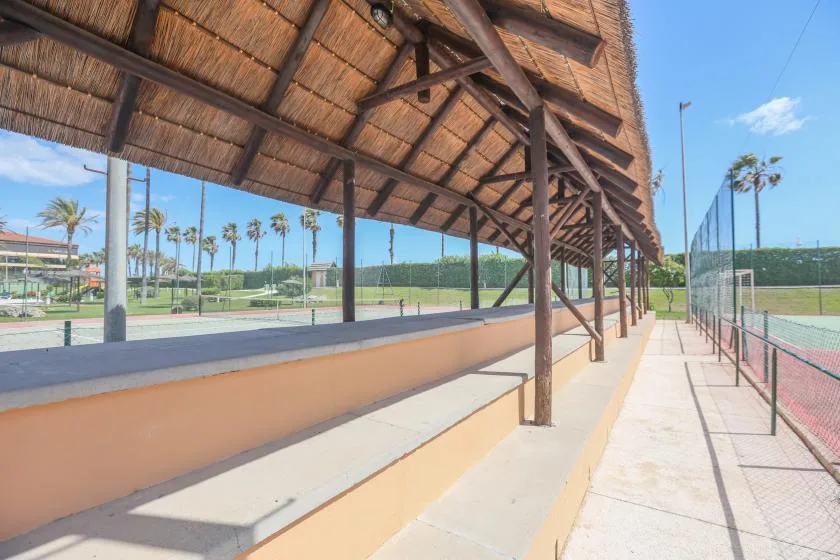 A covered sports-court viewing area with tiered seating beside the tennis court.