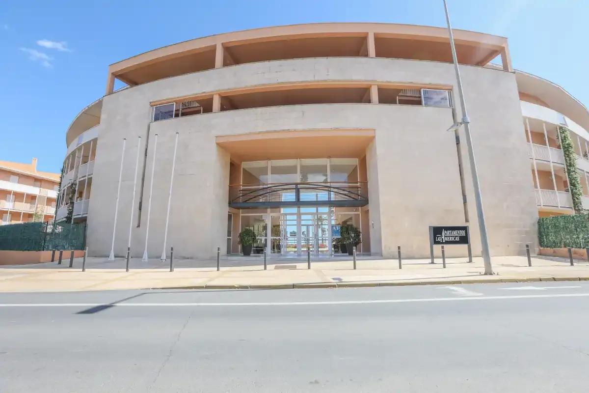 A modern curved building with a glass entrance faces a paved street.