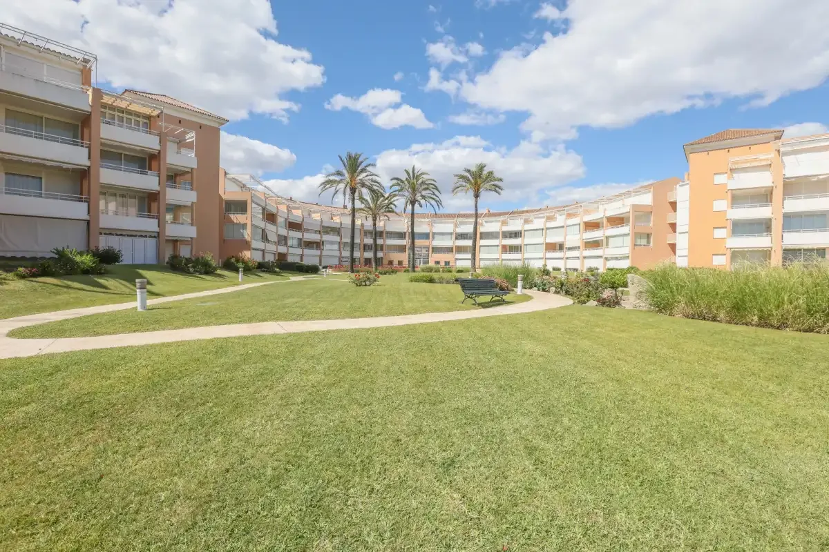 A landscaped courtyard with a lawn, curving path, palm trees, and surrounding apartment buildings.