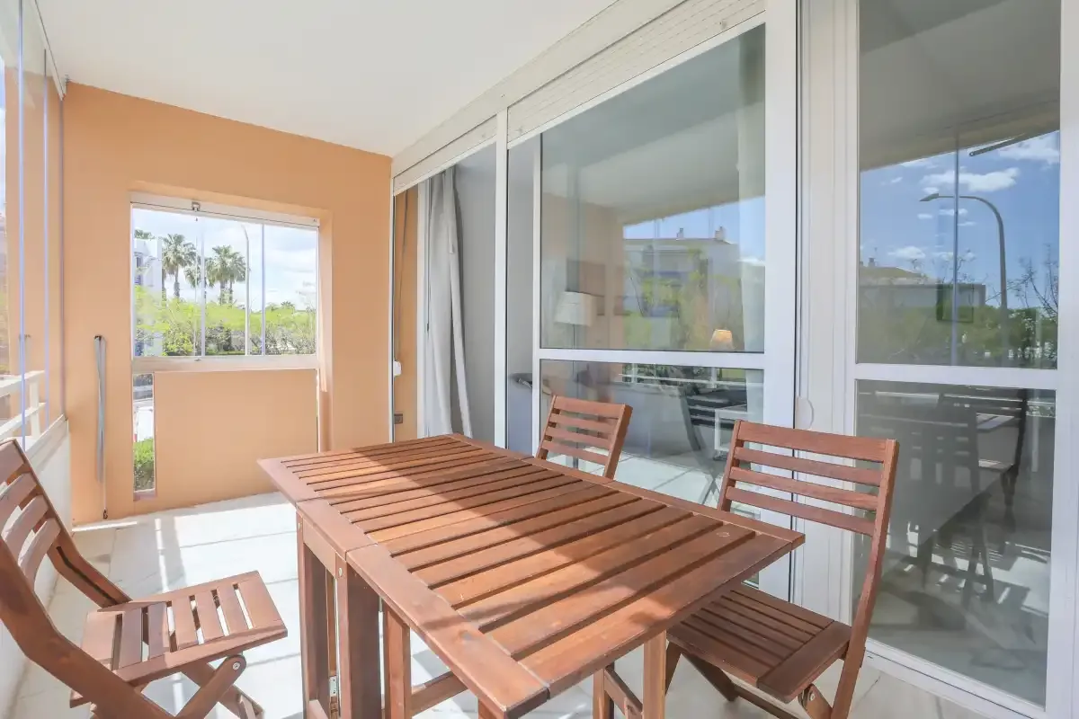 A balcony dining area with a wooden table and chairs beside large sliding glass doors.