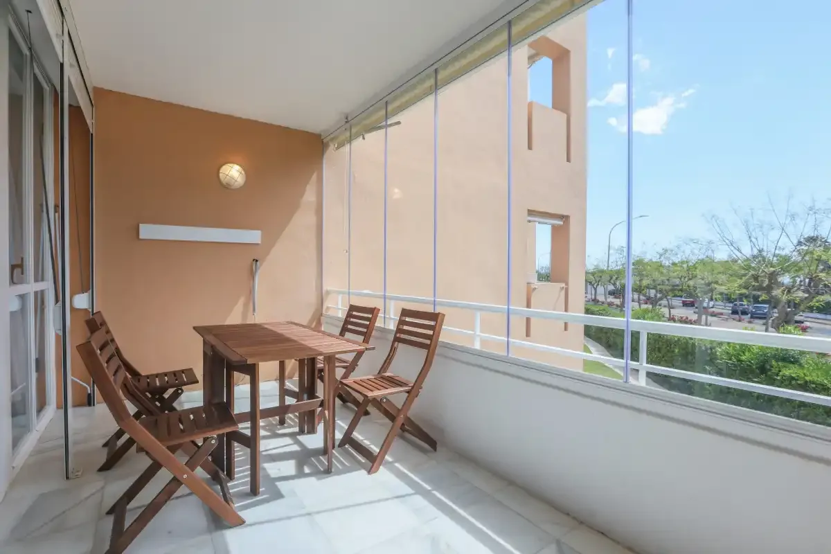 A glazed balcony dining area with a wooden table and seating.