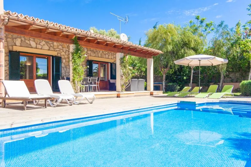 A swimming pool beside a stone house, with loungers arranged along the patio.