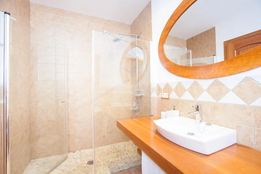 Un baño alicatado tiene una zona de ducha de vidrio y un lavabo sobre una encimera naranja.