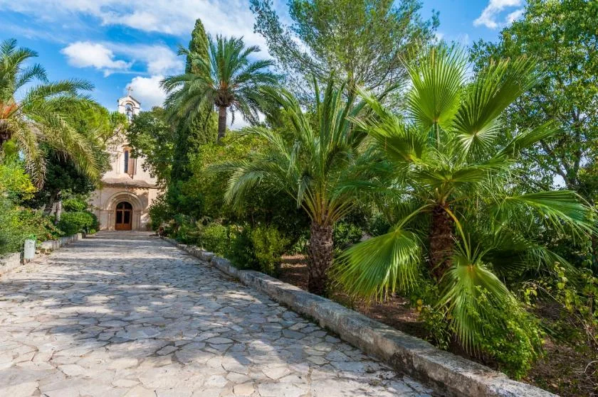 Un camino de piedra atraviesa una vegetación frondosa y conduce a un pequeño edificio con arco.
