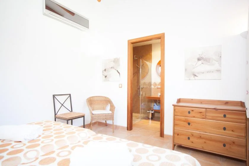 Un dormitorio luminoso con una cama, asientos y una puerta abierta al baño.