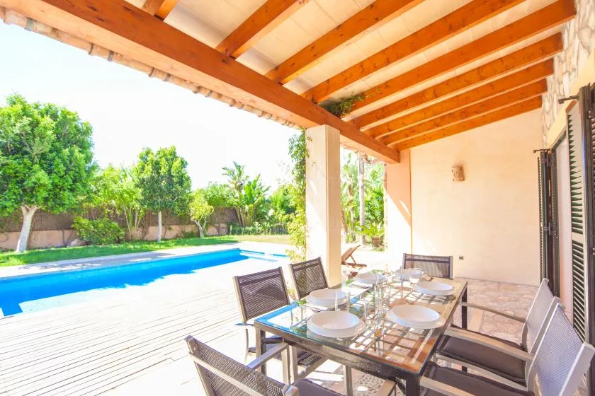 A covered patio with an outdoor dining table beside a swimming pool.