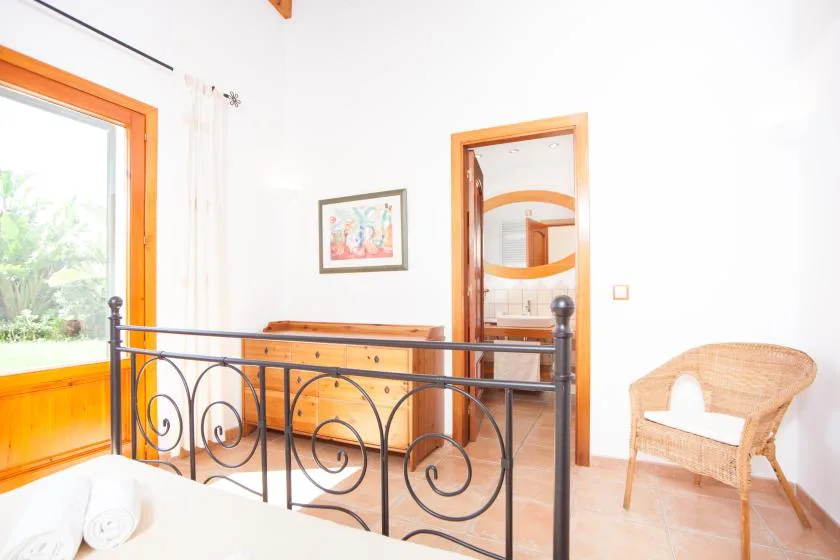Un dormitorio luminoso tiene una estructura de cama de metal oscuro y una silla de mimbre junto a la puerta.