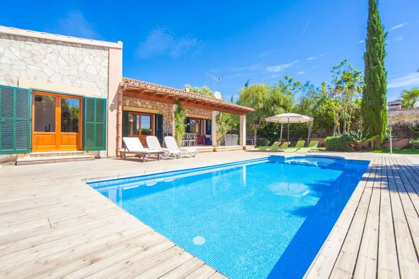 Piscina al aire libre junto a una casa de piedra, con terraza de madera y asientos.