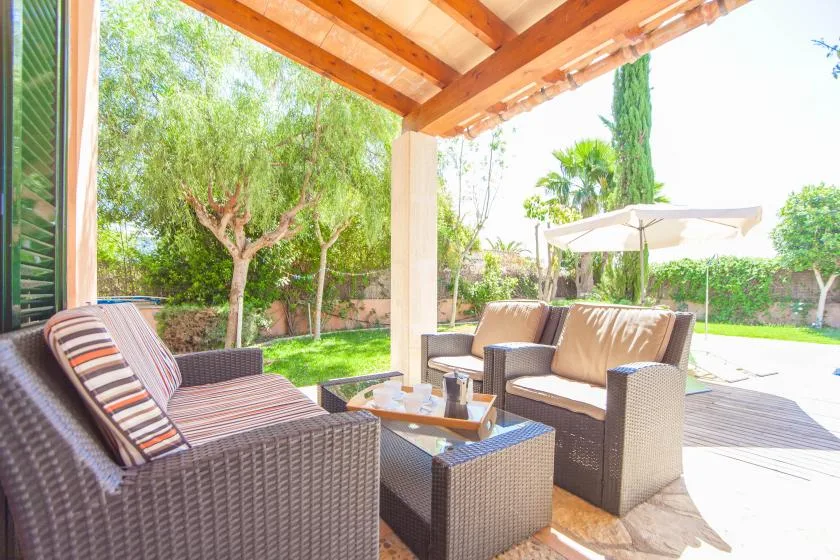 Un patio cubierto tiene asientos de mimbre alrededor de una mesa baja, con vistas a un jardín.
