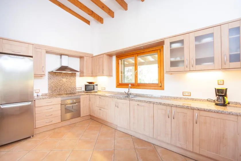 Una cocina luminosa con armarios claros, suelo de baldosas y una ventana sobre la encimera.