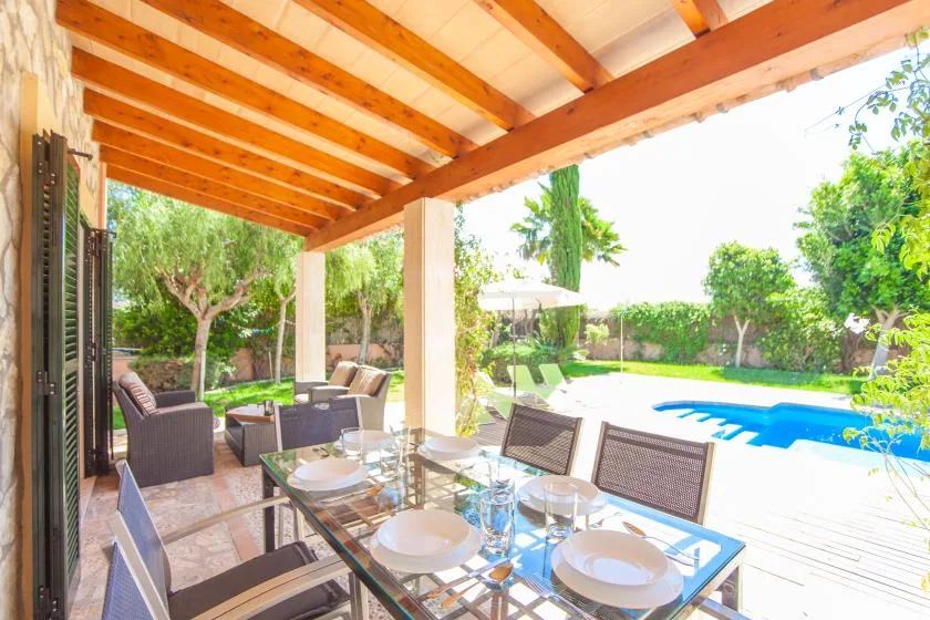 Una zona de comedor exterior cubierta da a una piscina y un jardín.