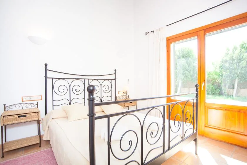 Un dormitorio luminoso con una cama junto a una ventana grande con vistas a la vegetación.