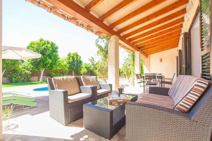 Una zona de estar cubierta da a una piscina y un jardín.