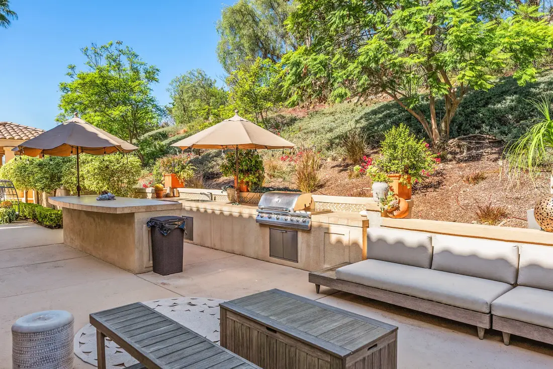 An outdoor patio with a built-in grill, shaded seating, and a landscaped hillside.