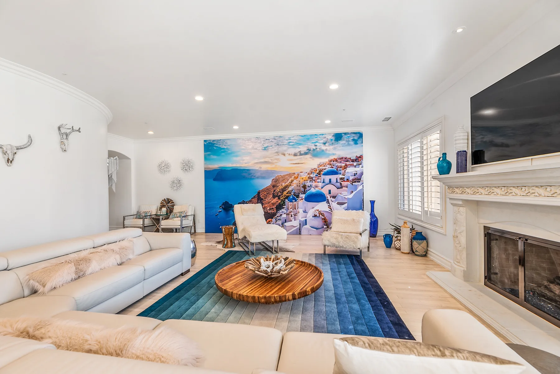 A bright living room with seating around a round wooden coffee table and a large coastal mural.