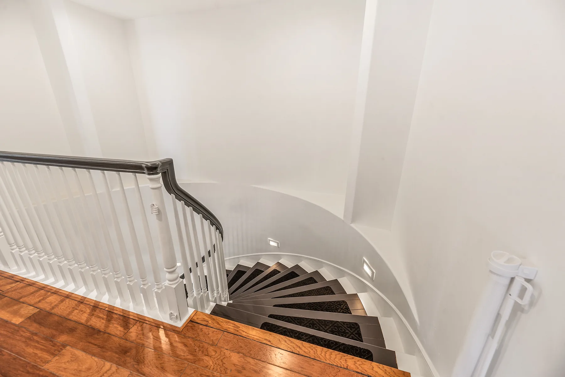 A curved staircase descends beside a white railing and wooden floor.