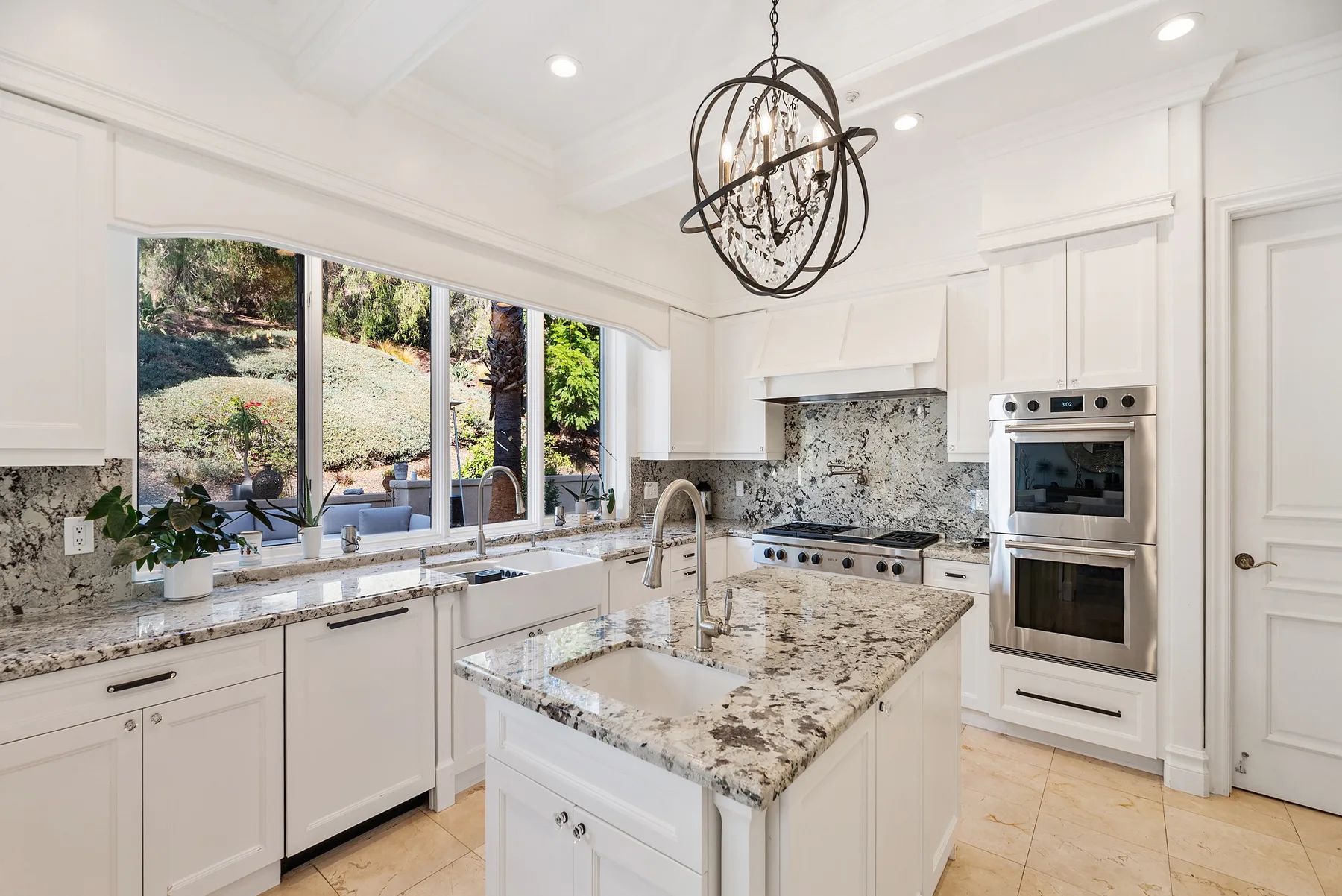 A bright kitchen with white cabinets, stone countertops, and a large central island.