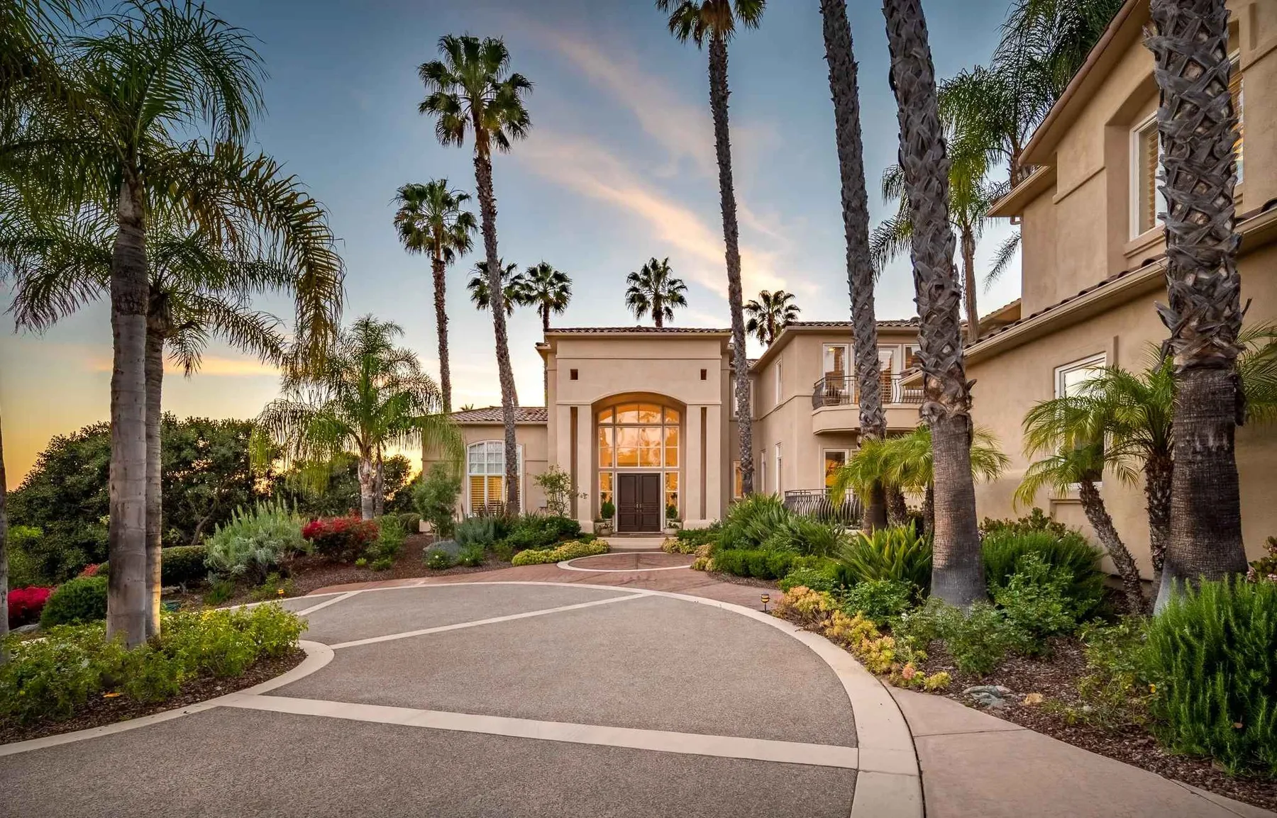 A landscaped driveway curves toward a large building among palm trees.