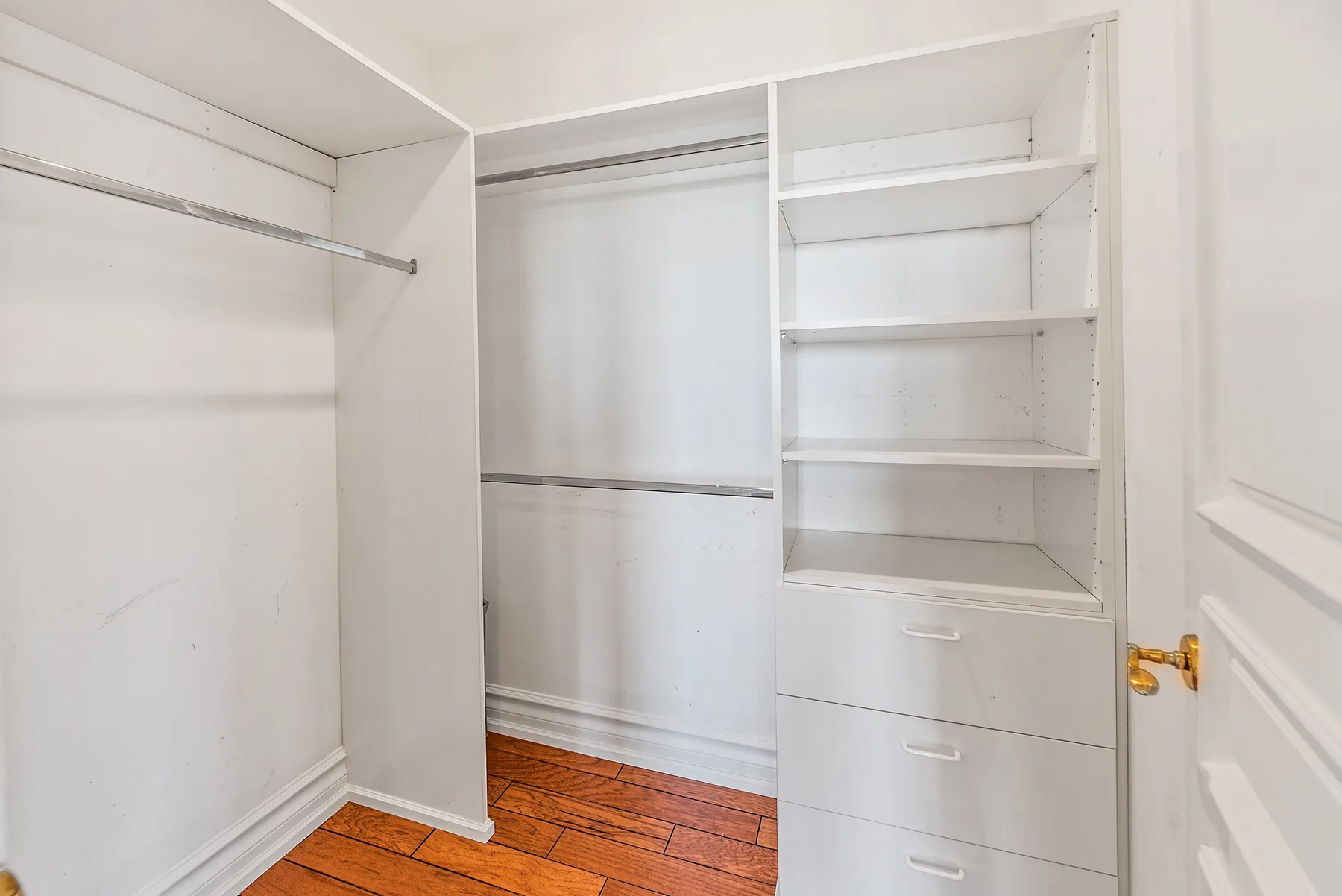 A white walk-in closet with open shelving, hanging space, and drawers.