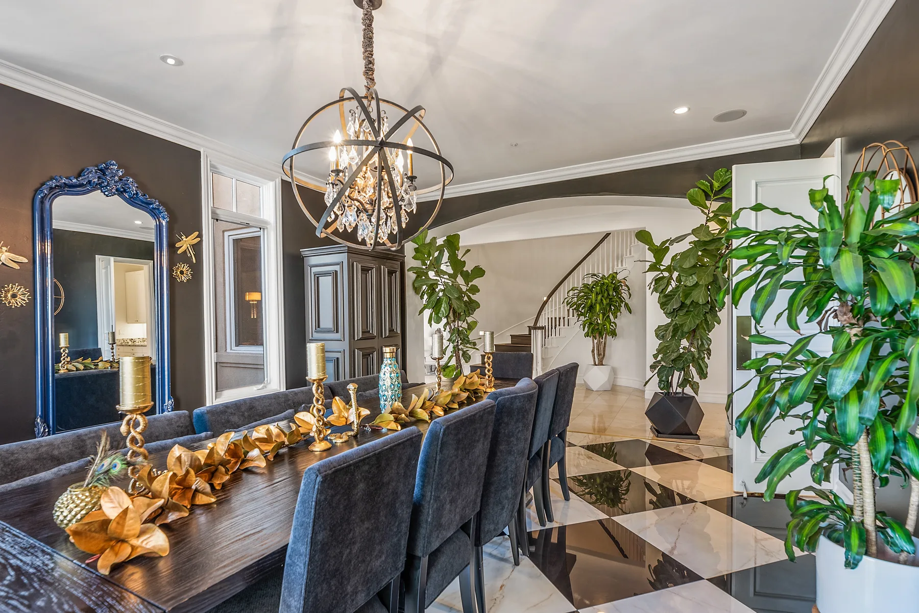 An elegant dining area with a long table, upholstered seating, and leafy plants.