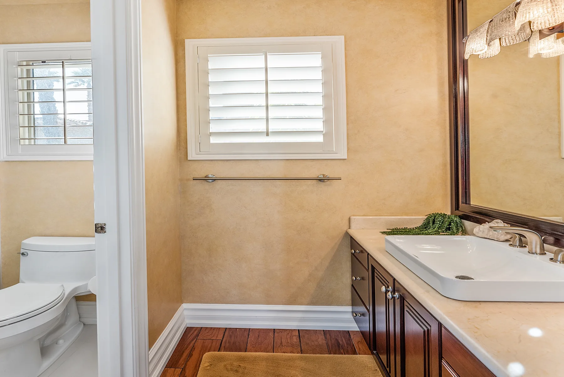A bathroom with a sink vanity, mirror, and a window above a toilet.