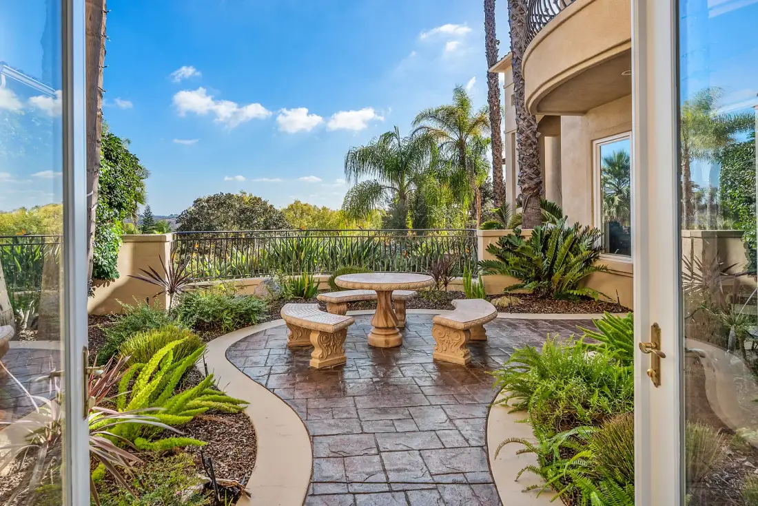 A landscaped patio with a round table and surrounding seating overlooks greenery.