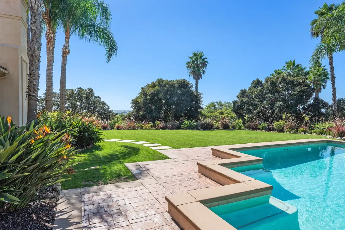 A landscaped garden with a swimming pool and paved patio.