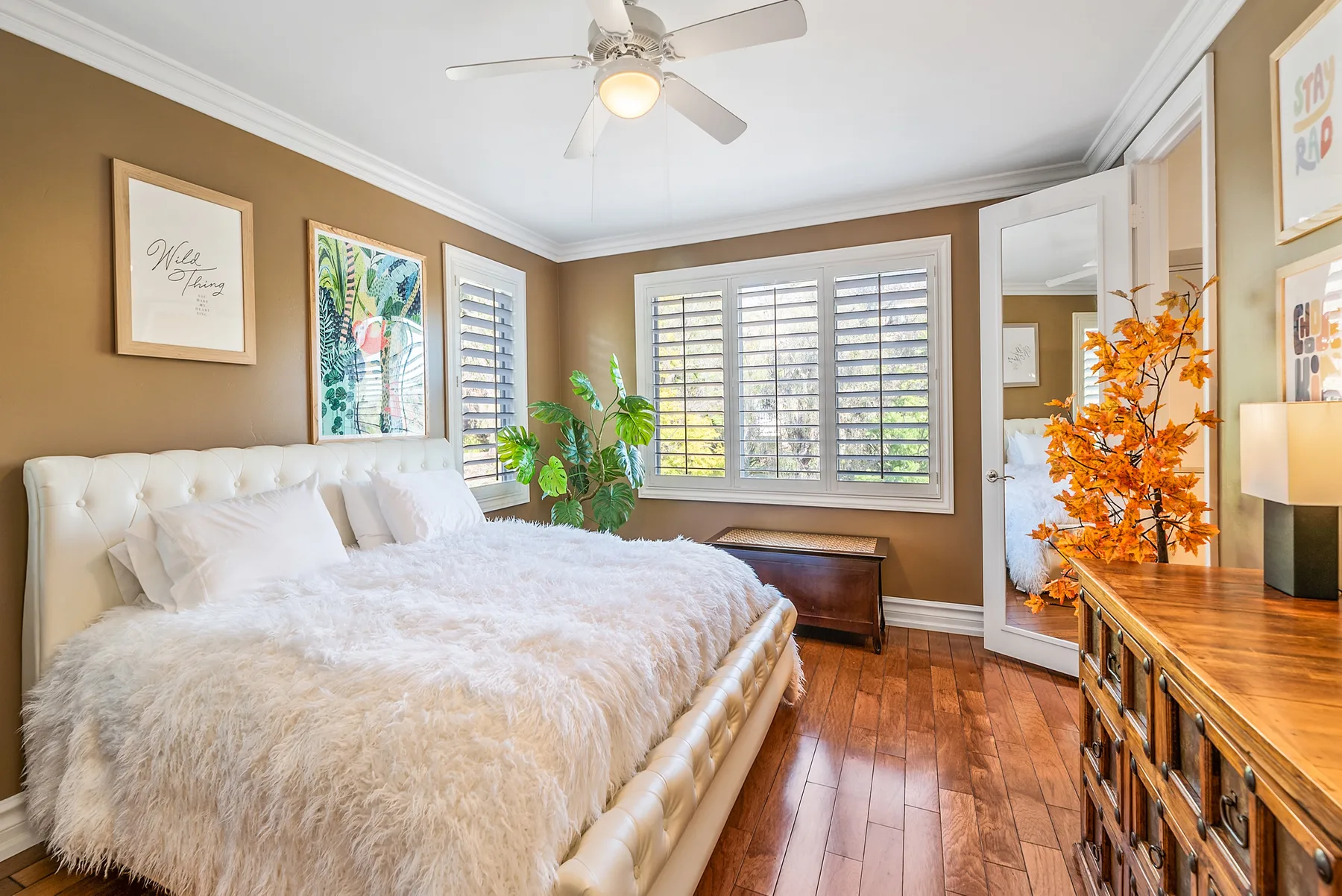 A bedroom with a bed, shuttered windows, and a wooden dresser.
