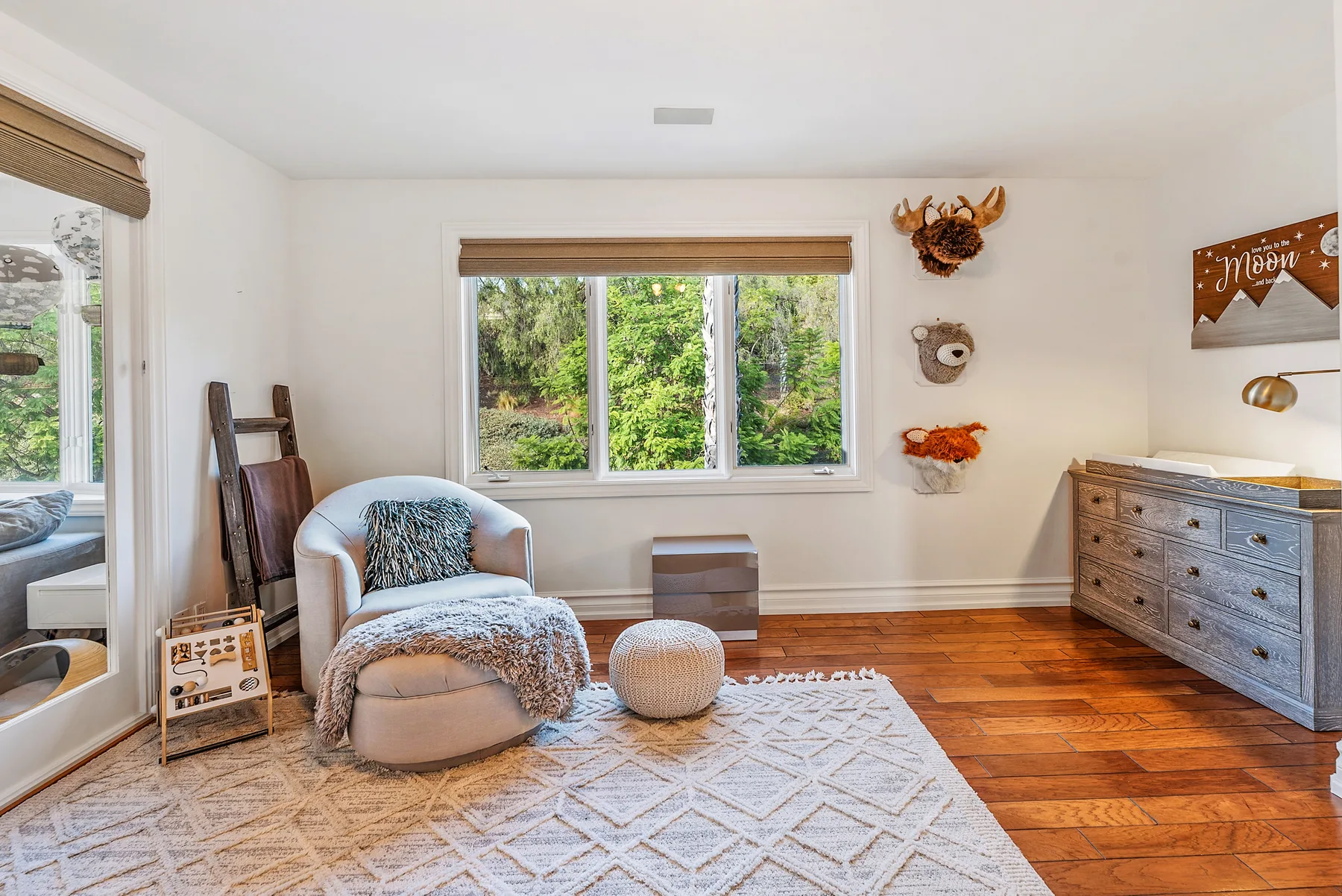 A bright sitting room with an armchair, rug, and windows overlooking greenery.