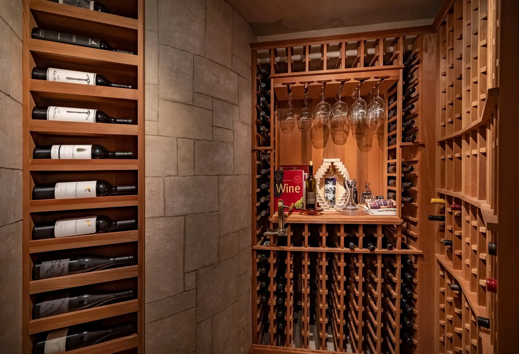 A wine cellar with wooden bottle racks and hanging wine glasses.