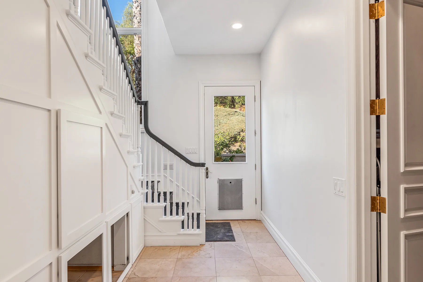 A bright entry hall with a staircase and a glazed exterior door.