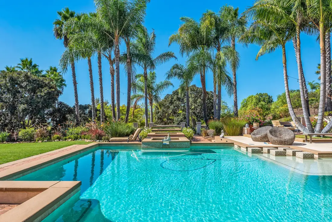 A swimming pool sits among palm trees and landscaped greenery.