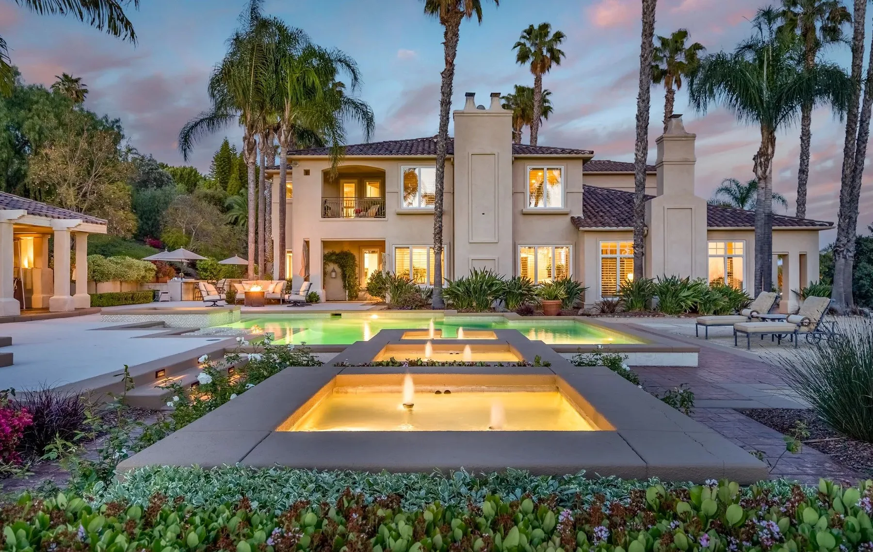 A landscaped villa exterior with a lit courtyard pool at dusk.