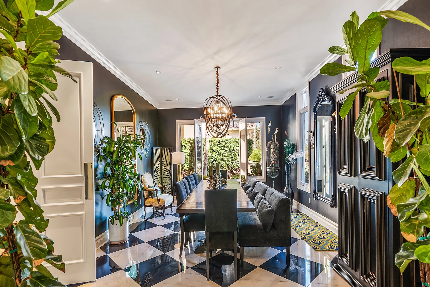 A dining area with a long table, dark seating, and several leafy plants.