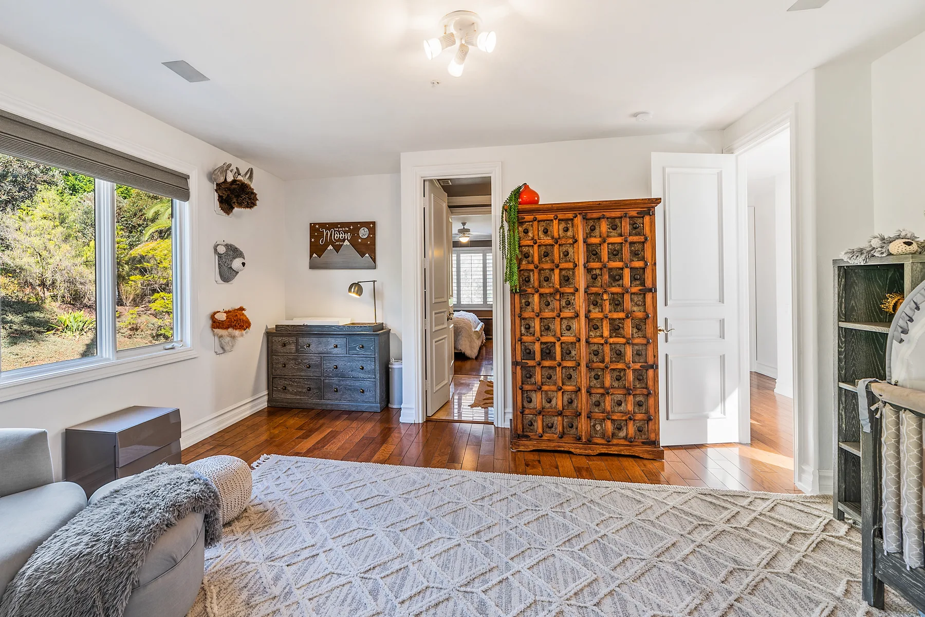 A bright living room with a patterned rug and an ornate wooden cabinet.