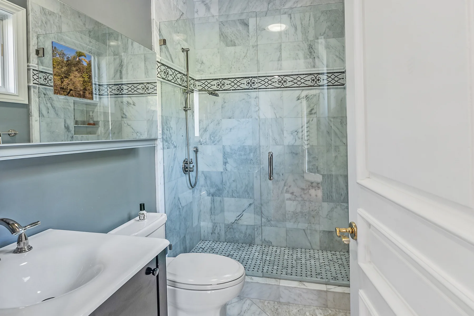 A bathroom with a glass shower, tiled walls, a sink, and a toilet.