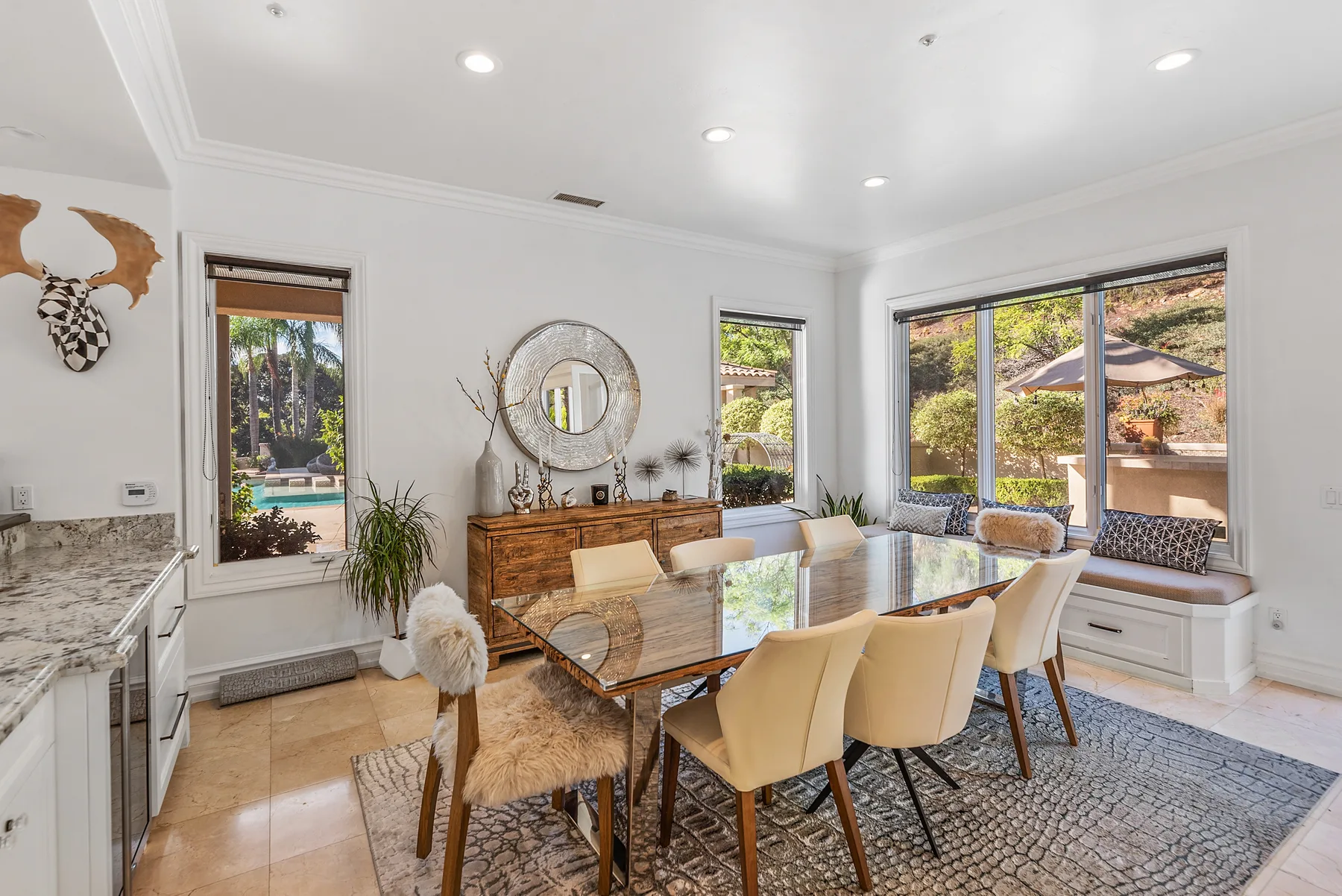 A bright dining area has a long table beside large windows and a built-in bench.