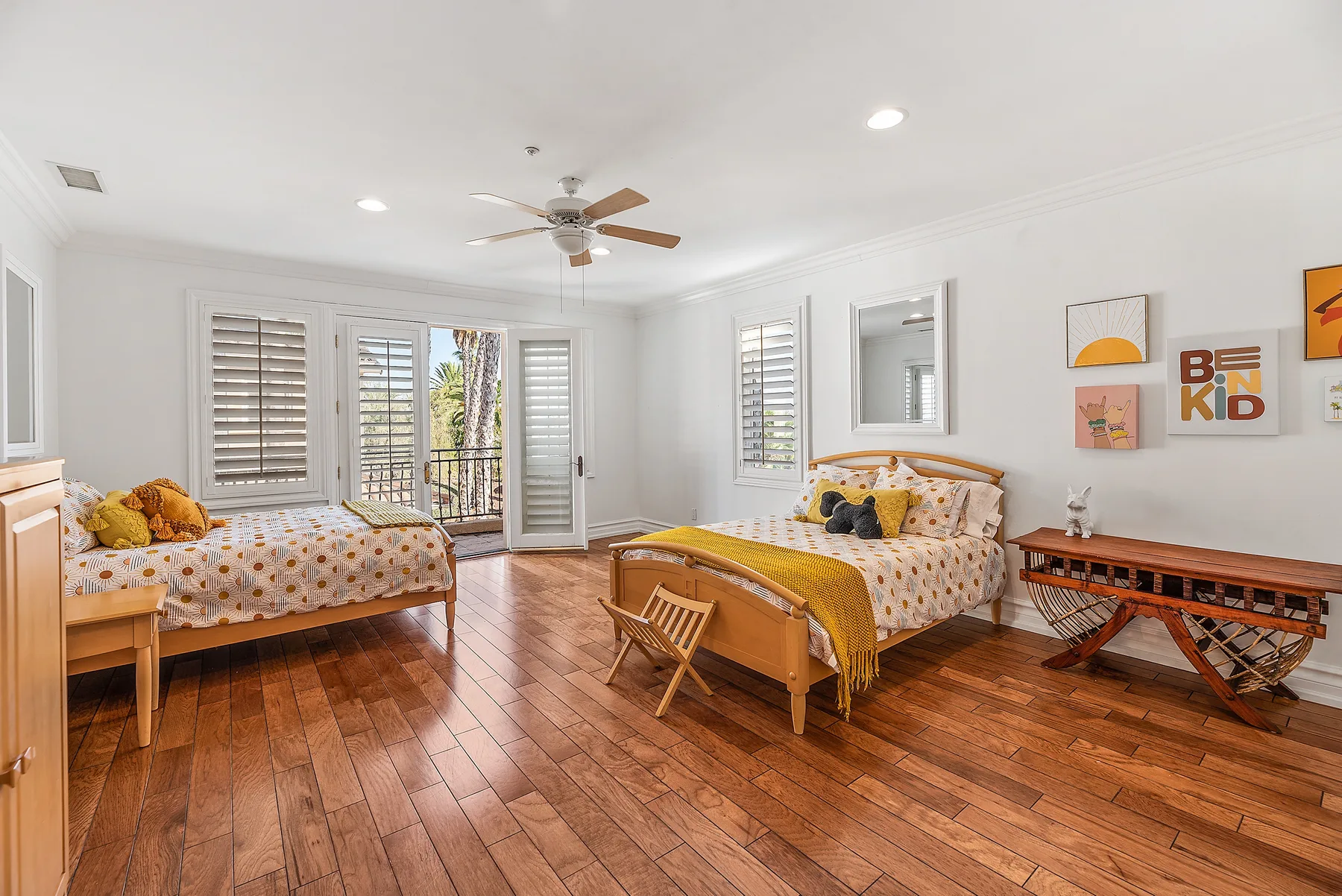 A bright bedroom with two beds, wooden flooring, and a ceiling fan.