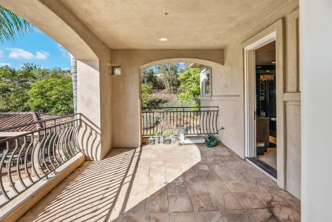 A covered outdoor terrace with tiled flooring and a metal railing overlooks greenery.