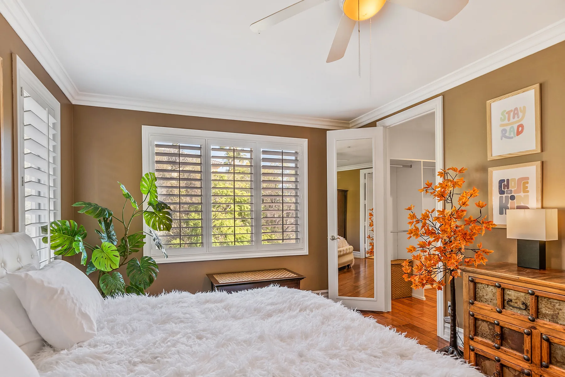 A bedroom with a bed, shuttered windows, and leafy plants.