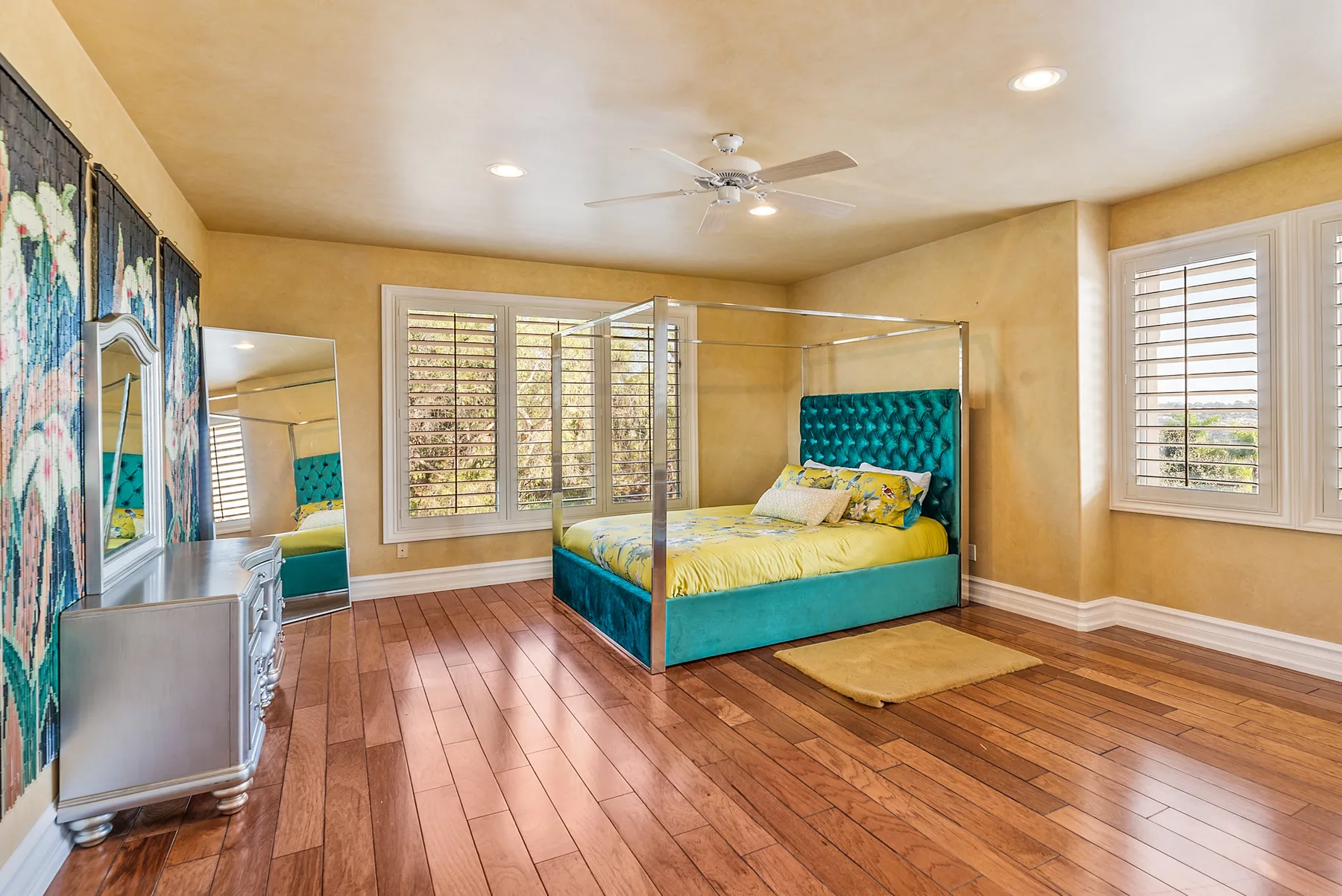 A bedroom with a teal bed, canopy frame, and wood flooring.