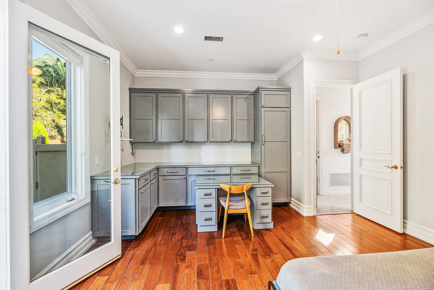 A bright room with gray cabinets, a desk, and a wooden floor.