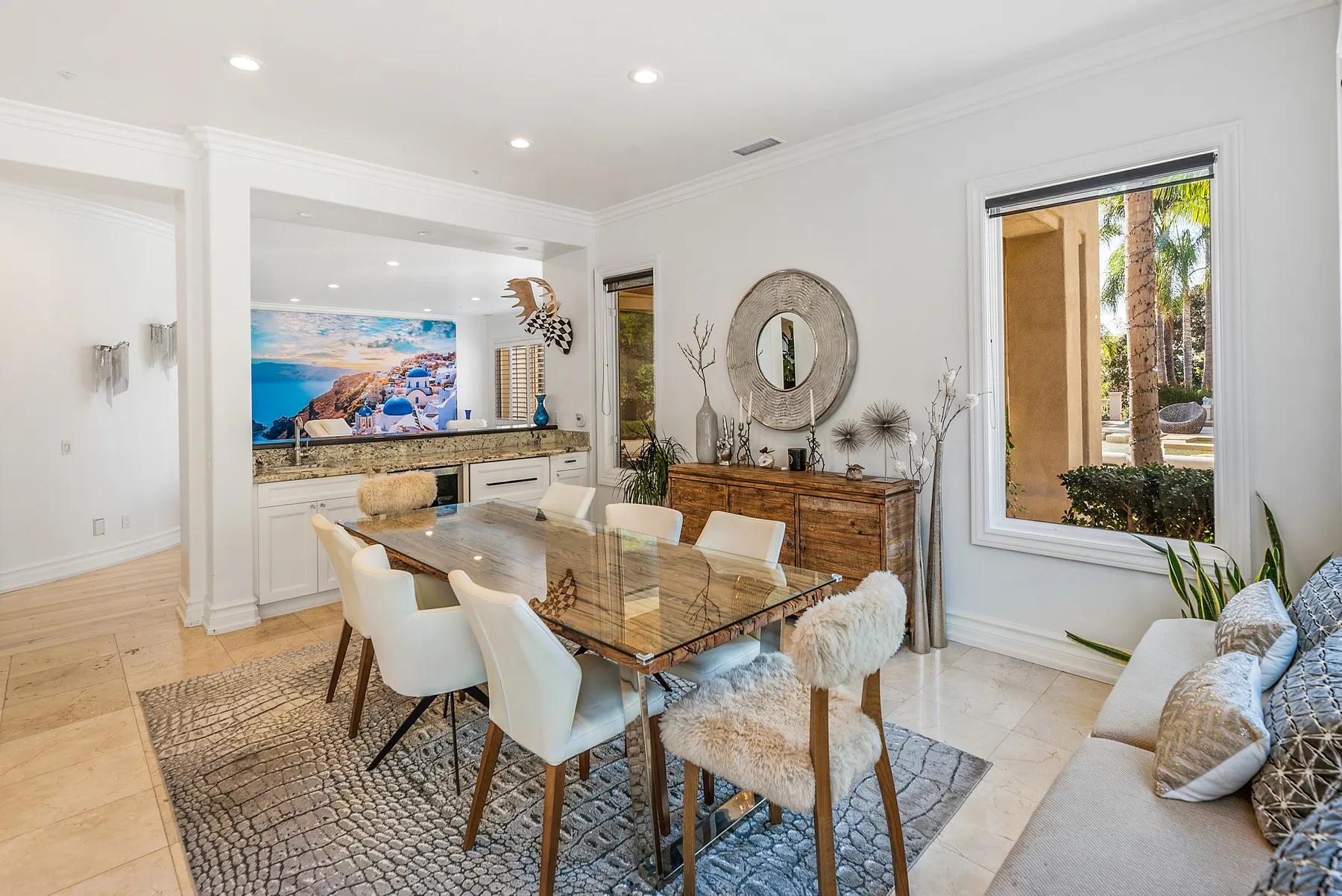 A bright dining and living area features a dining table, seating, and a wall-mounted television.