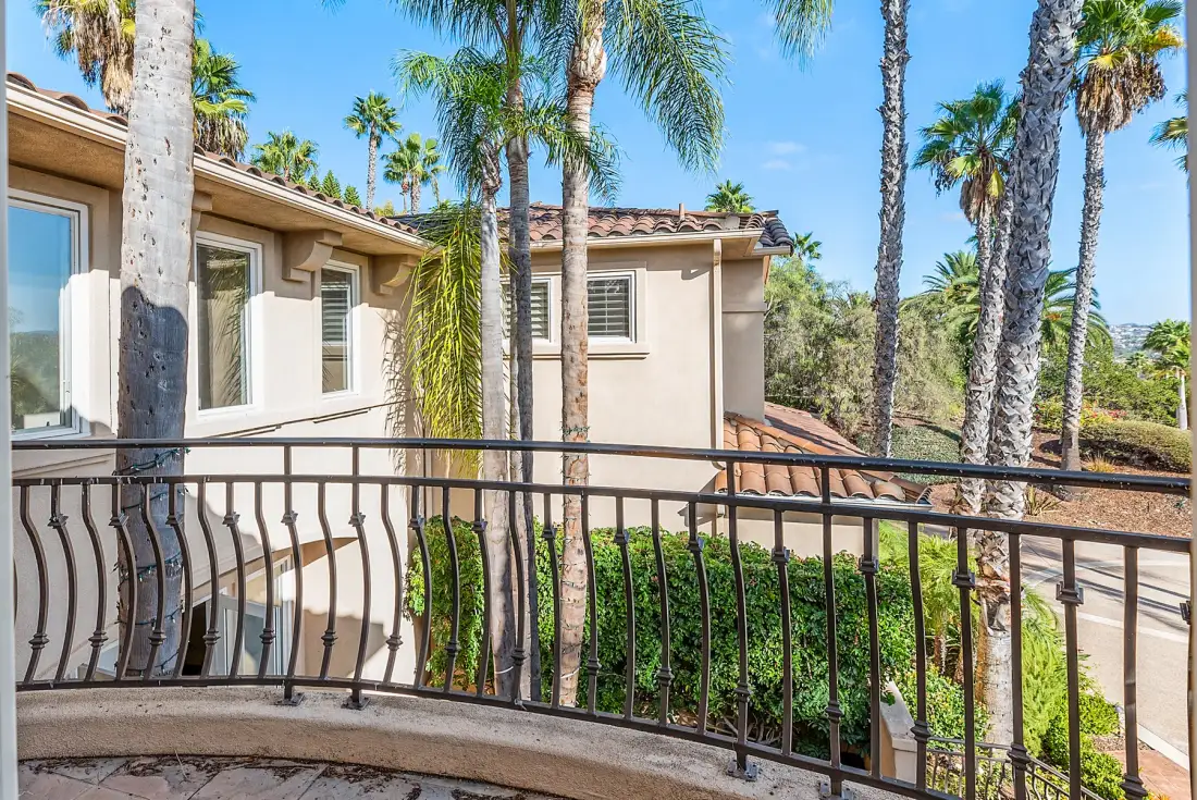 A curved balcony overlooks a beige building and several palm trees.