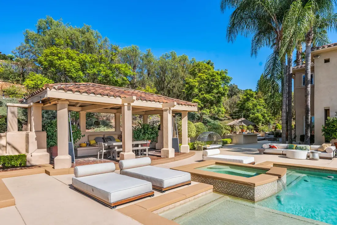An outdoor pool patio with a covered seating area and lounge cushions.